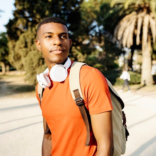Cropped shot of a young black man student with headphones and bag walking in public park