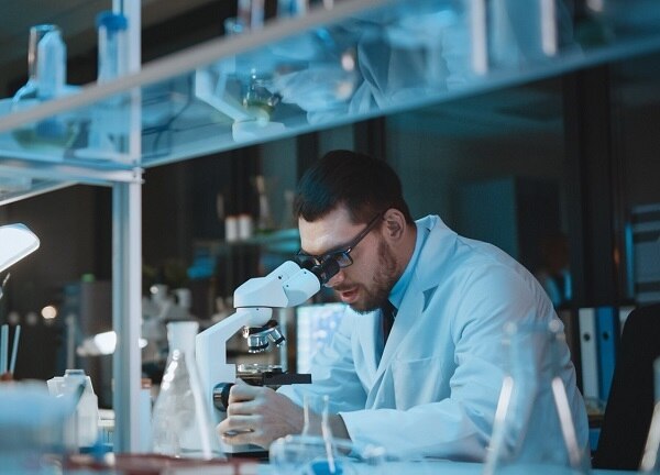 Medical Development Laboratory: Caucasian Female Scientist Looking Under Microscope, Analyzes Petri Dish Sample. Specialists Working on Medicine, Biotechnology Research in Advanced Laboratory
