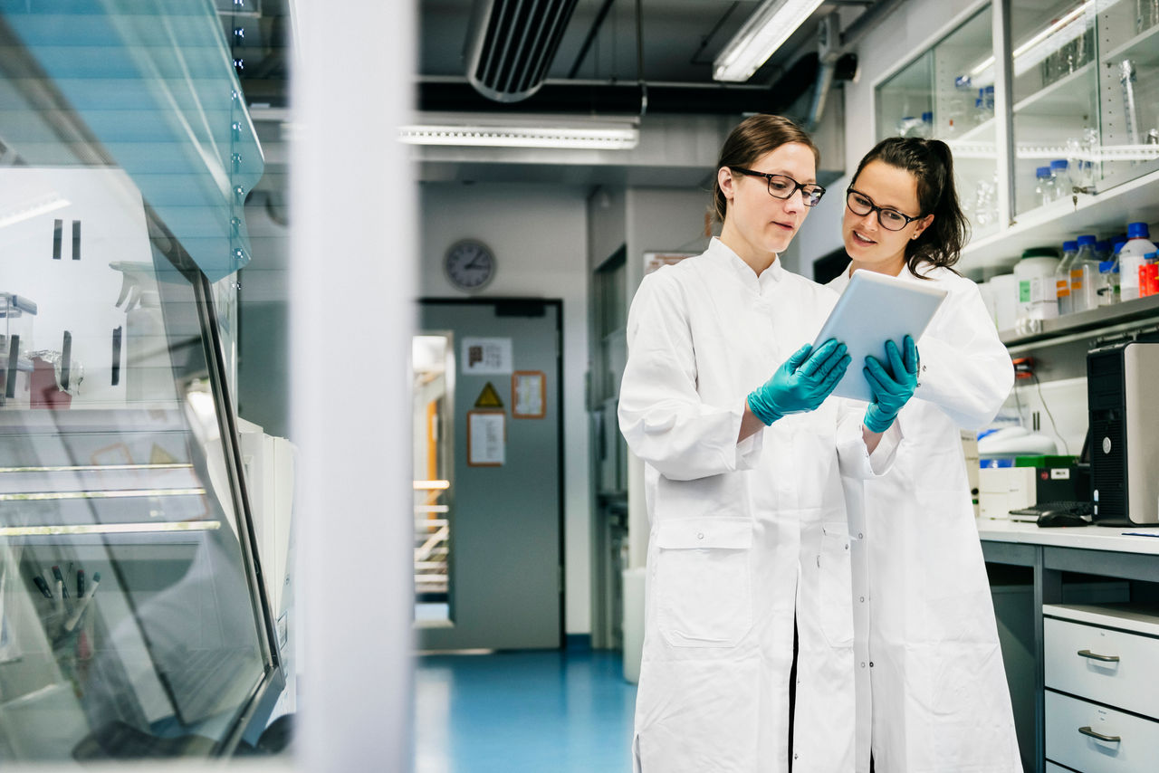 Two scientists standing in the laboratory and discussing data from experiment together.