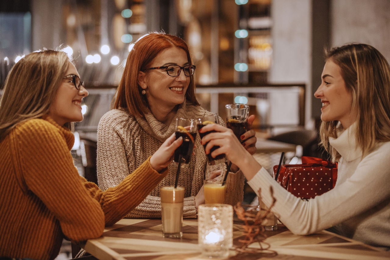 Mother and her two adult daughters are toasting with coke while relaxing in a cafe.