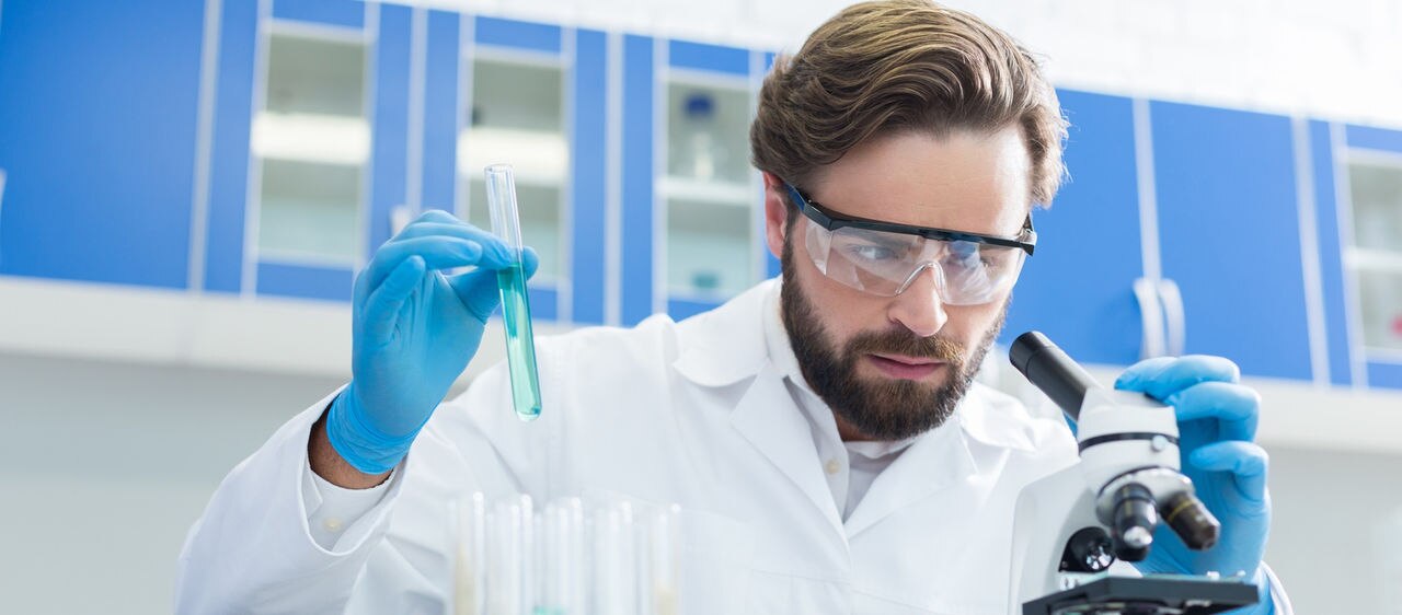 Modern science. Serious intelligent pleasant man sitting at the table and holding a test tube while working in the lab