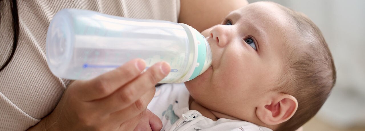 Close up view of a mother feeding her baby son with a bottle of milk.