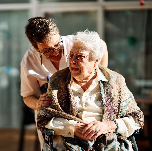 Nursing assistant taking care of senior woman in wheelchair in a nursing home