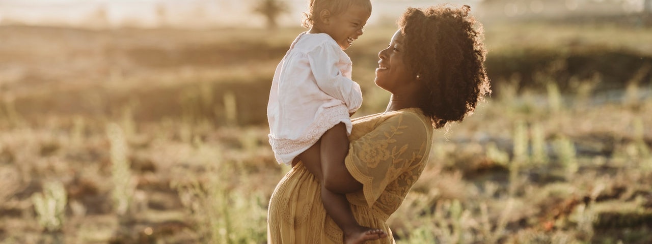 A pregnant African woman with her hands on her back smiling into the distance.