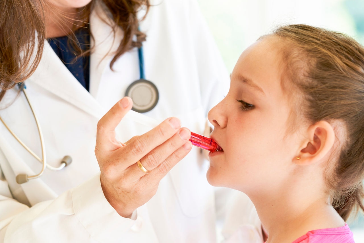 Close up of a little girl getting medicine in a syringe with red liquid by a pediatrician