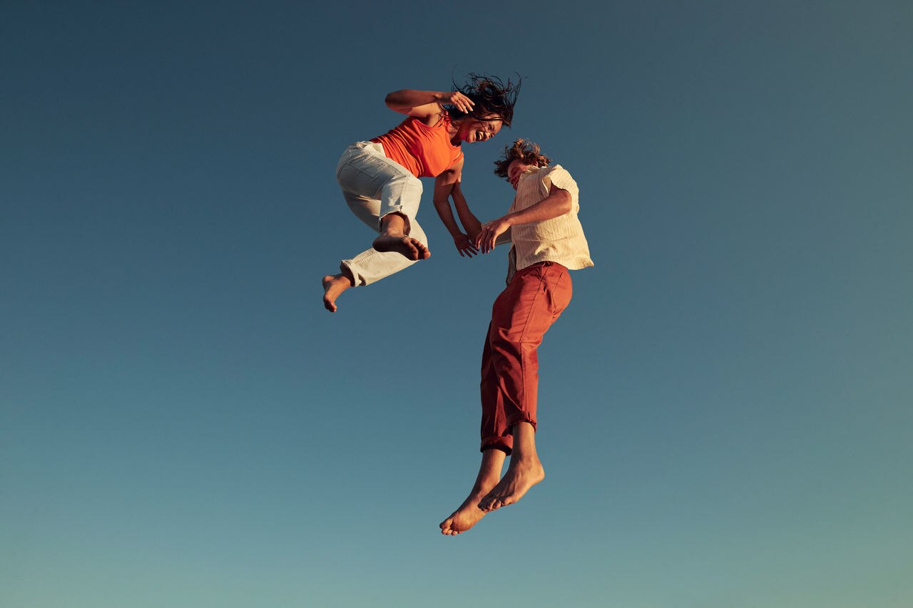 Low angle view of cheerful friends jumping high up in mid-air against clear blue sky