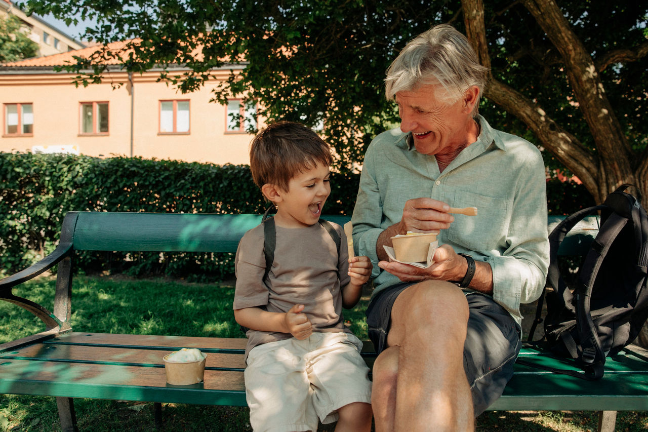 Happy grandfather and grandson enjoying ice cream while sitting on bench; Shutterstock ID 2213915861; purchase_order: TTH_1st round (12 images); job: ; client: ; other: 