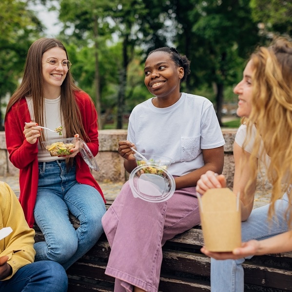 Small group of diverse friends having fun eating healthy take out food in the park