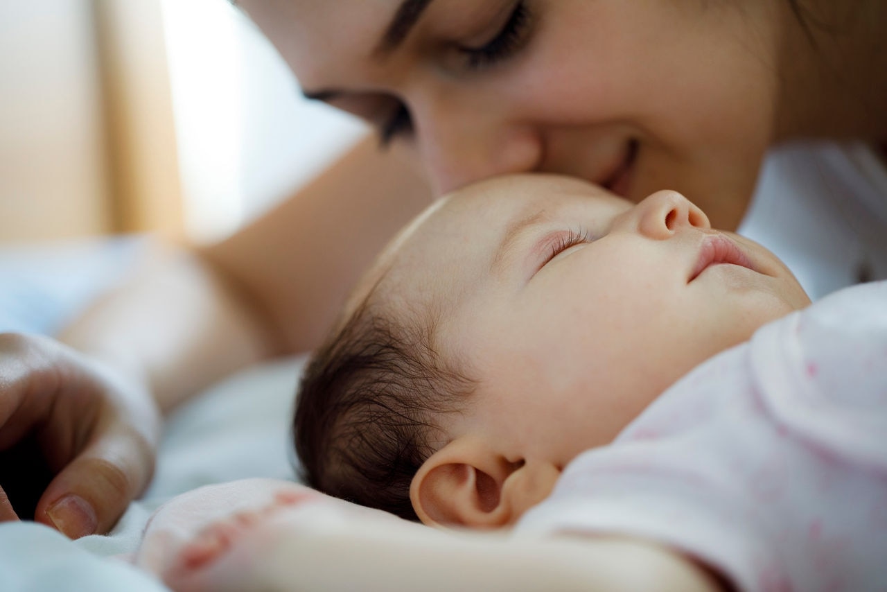 Mother kissing her sleeping newborn baby