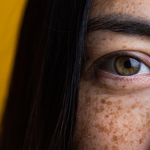 Close up on green eyes of beautiful Asian woman with freckles, looking at camera.