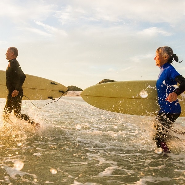 Senior couple (aged65-69) enjoying a surf together in the sea at sunset