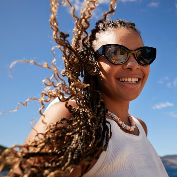 Smiling young woman wearing sunglasses with tousled braided hair in wind on sunny day