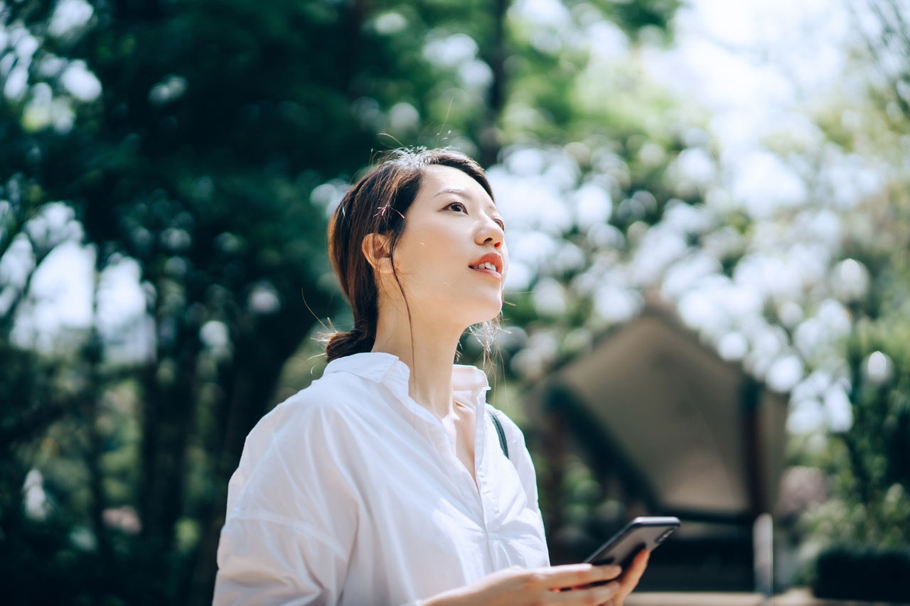 Young Asian woman using smartphone outdoors in the nature.