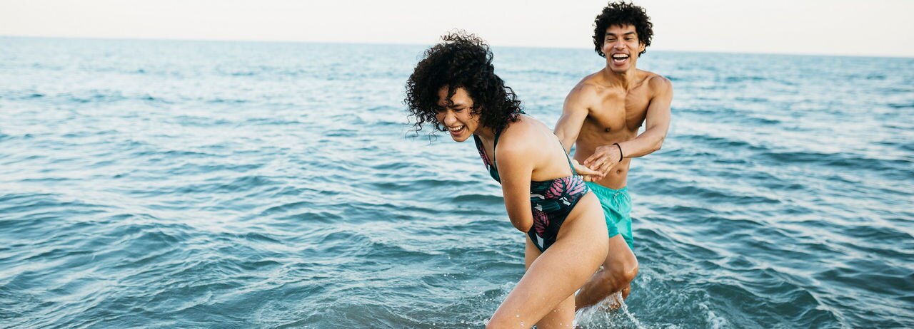 Young latin woman and a black man wearing swimsuit in the sea playing together at the water's edge