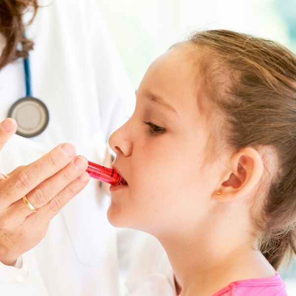 Close up of a little girl getting medicine in a syringe with red liquid by a pediatrician