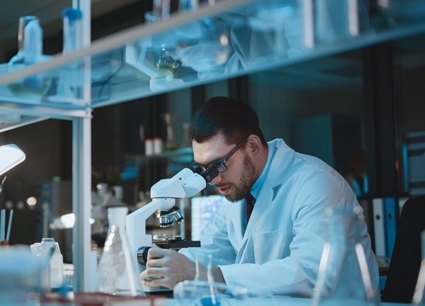 Medical Development Laboratory: Caucasian Female Scientist Looking Under Microscope, Analyzes Petri Dish Sample. Specialists Working on Medicine, Biotechnology Research in Advanced Laboratory