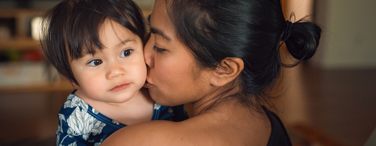 An Asian mother holding and kissing her mixed race toddler daughter.