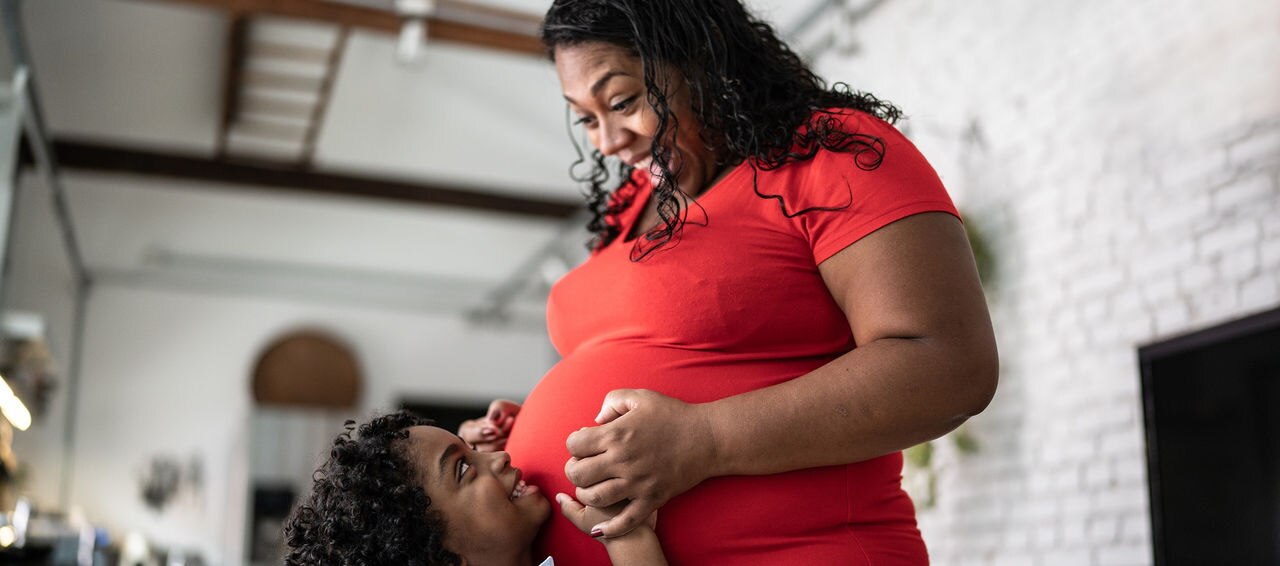 Young son putting hand on pregnant mothers stomach at home