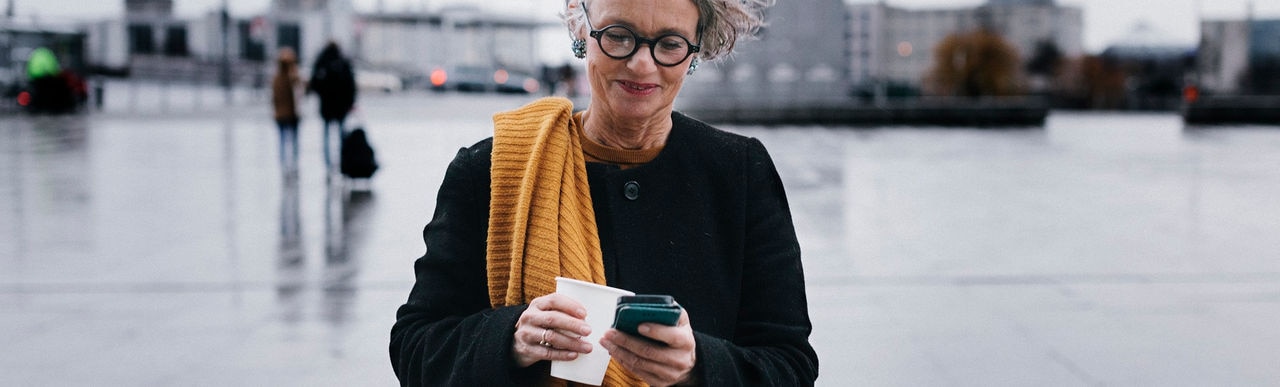A mature businesswoman siling while texting using her smartphone on her lunchbreak .