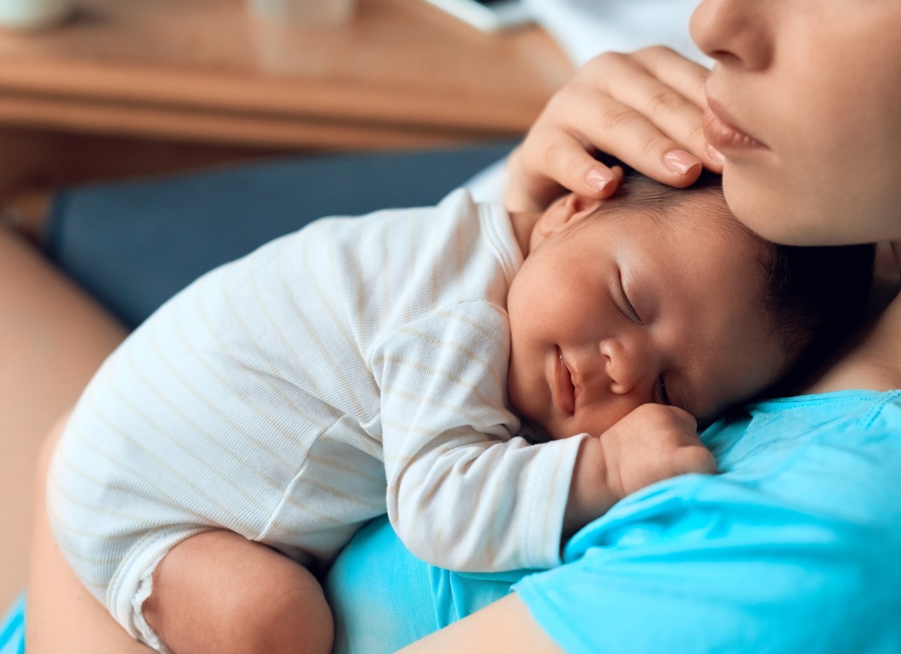 side view of innocent baby girl sleeping on her mother's chest, smiling and feeling relaxed.