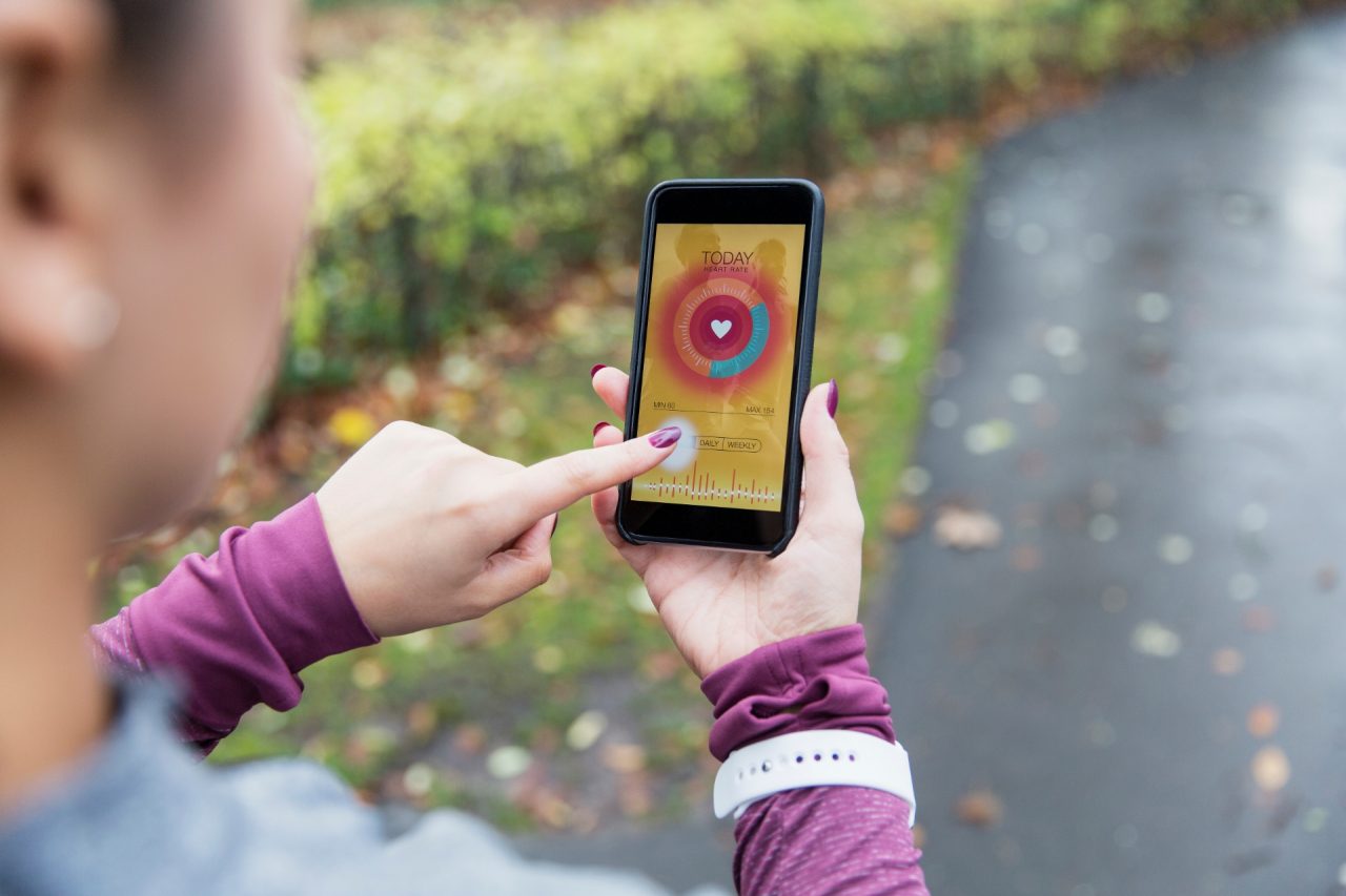 Female runner checking heart rate monitor on smart phone on path