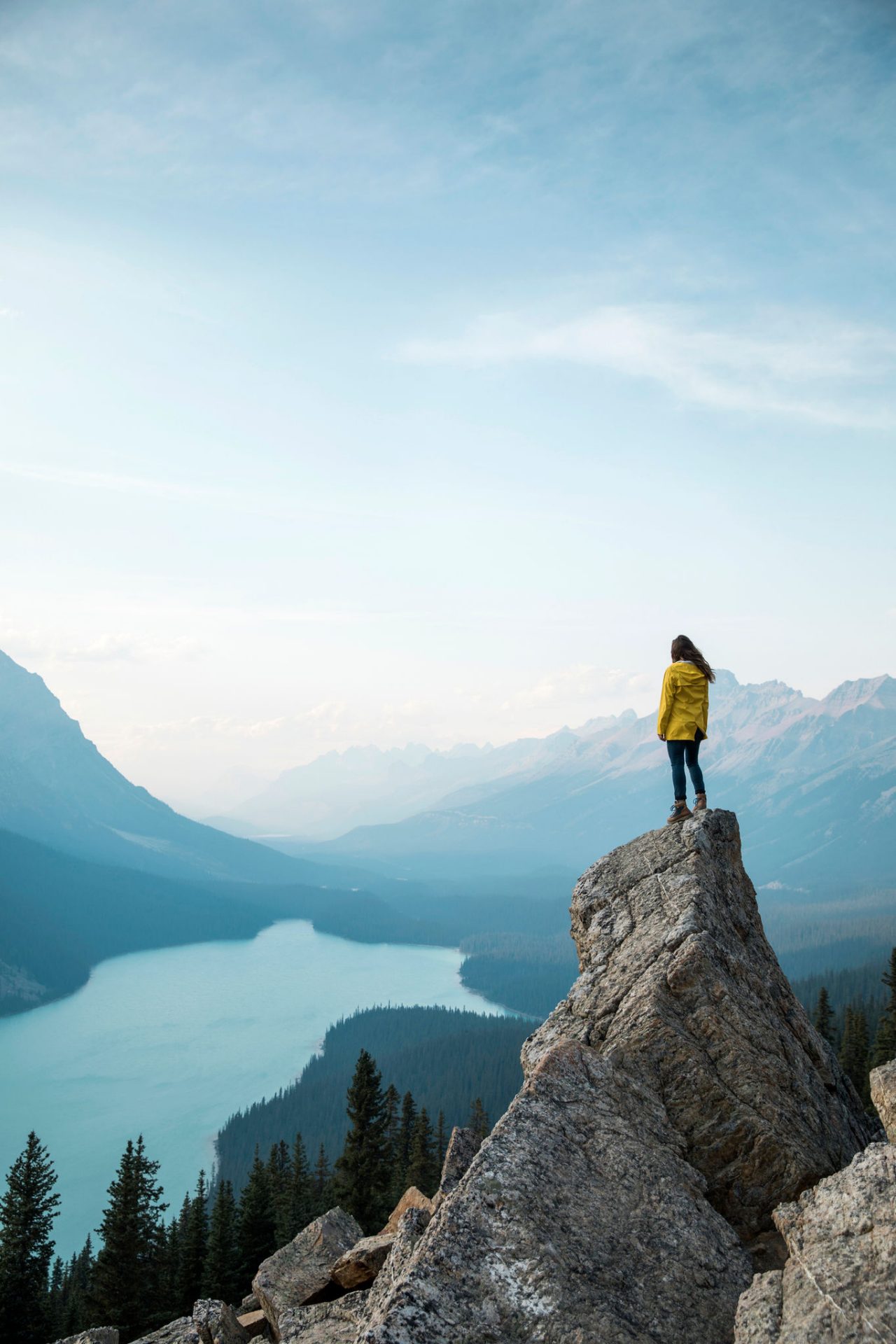 A young woman in a yellow jacket standing on a rock overlooking Peyto Lake.