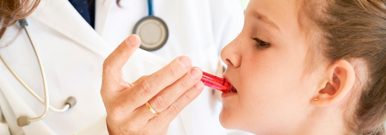 Close up of a little girl getting medicine in a syringe with red liquid by a pediatrician