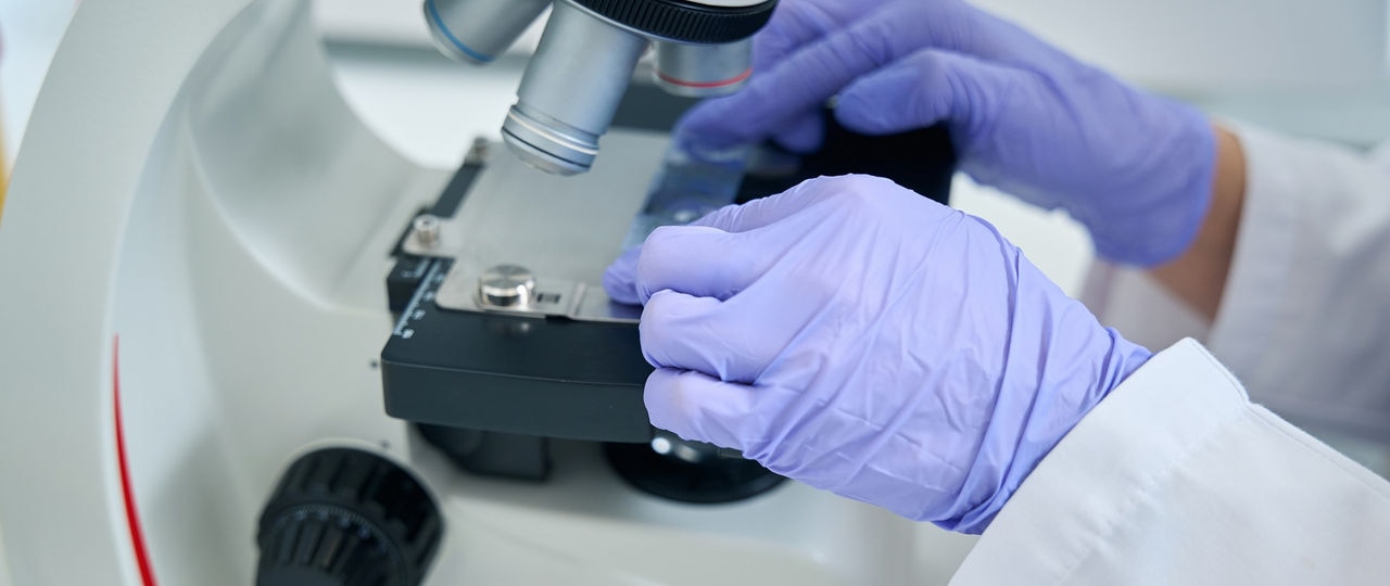 Geneticist laboratory assistant in the testing unit studies biomaterial for a dna test, a specialist uses a powerful microscope
