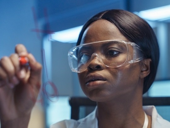 A young thoughtful African-American scientist writing formulas on  a glass board, we see her behind that board