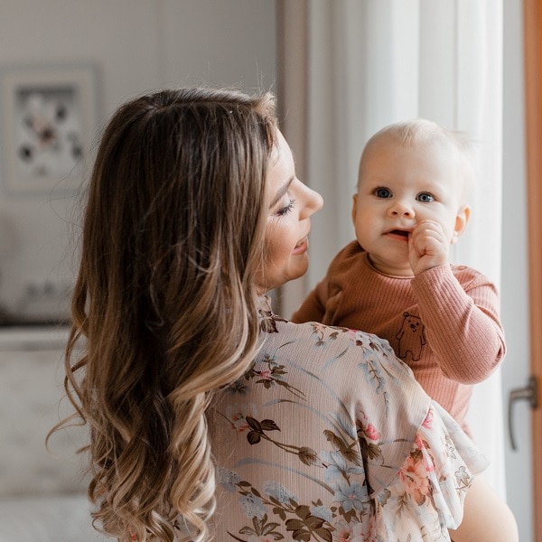 Young woman mom with baby girl on hands near window at home