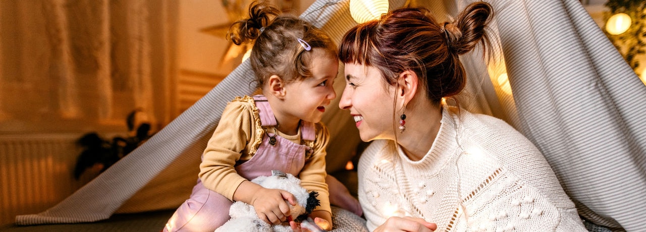 Mother and daughter are having fun reading a book under the illuminated tent in the bedroom.