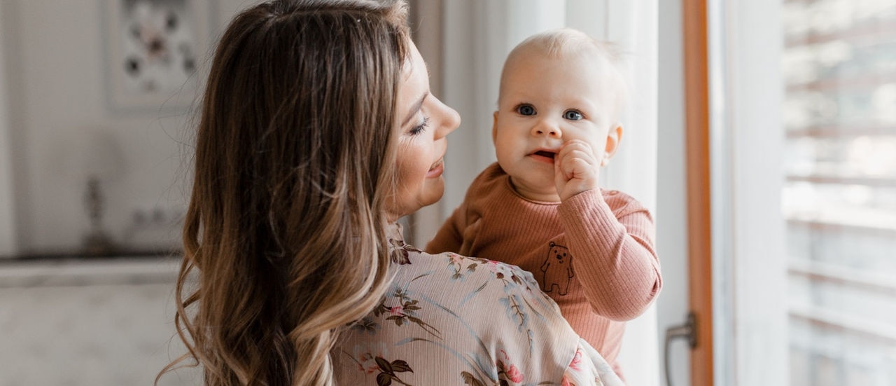 Young woman mom with baby girl on hands near window at home