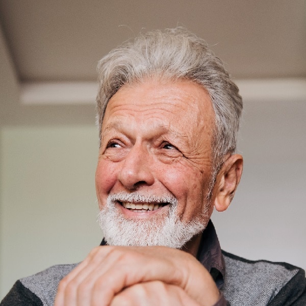 Portrait of a happy senior man with a beard sitting at home with a walking cane and smiling.