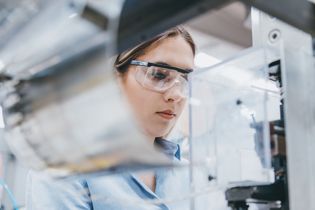 Professional young industrial factory woman employee working with machine parts putting, checking and testing industrial equipments cables in large Electric electronics wire and cable manufacturing plant factory warehouse