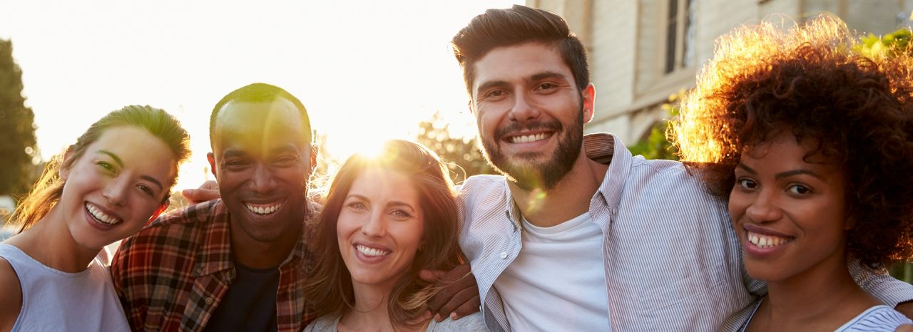 Group of smiling young adult friends embracing in the street