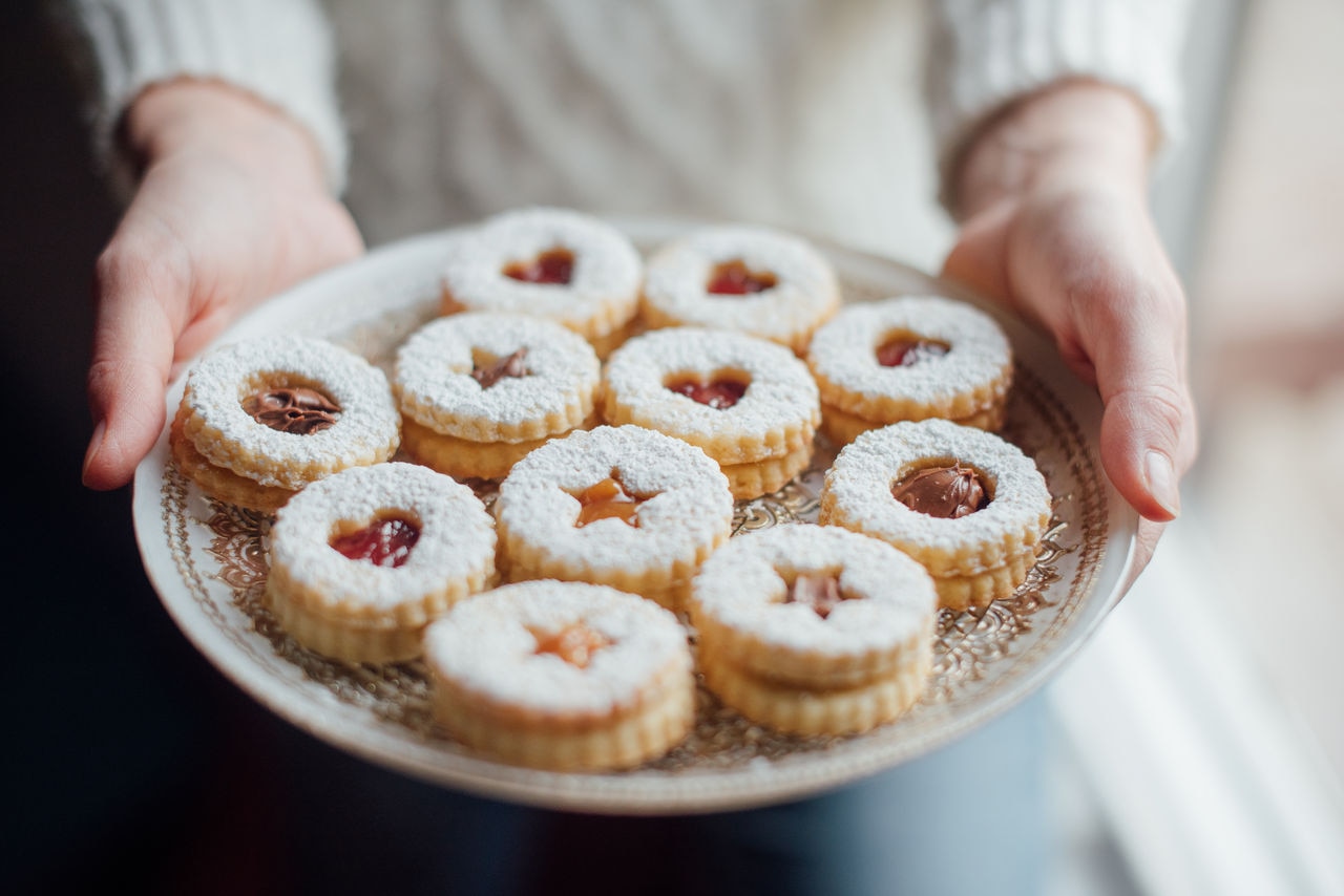 Close up of hands holding a plate with homemade Linzer Cookies.