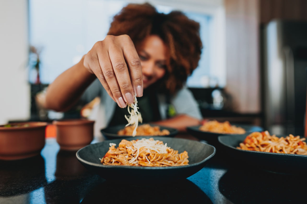 Woman putting grated cheese on macaroni