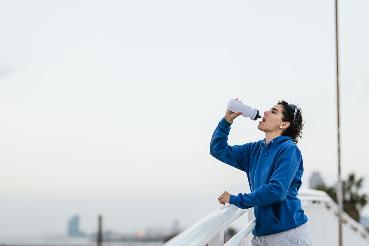 Athletic woman drinking water from a bottle after intense physical activity, exercising in the city to stay healthy.