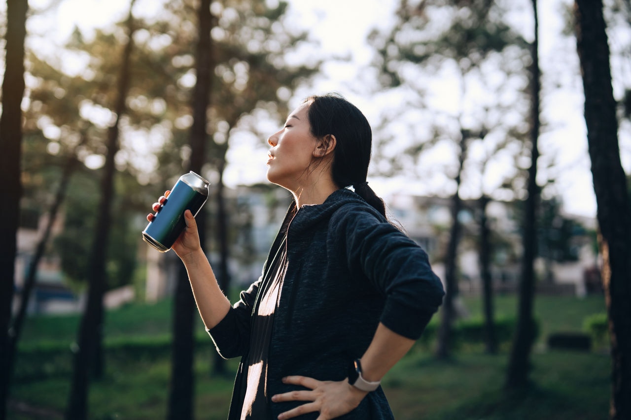 Young Asian sports woman taking a rest and drinking water from reusable water bottle after jogging outdoors in park. Taking water break. Staying hydrated. Fitness goal. Wellbeing and wellness. Health and fitness training routine. Healthy living lifestyle