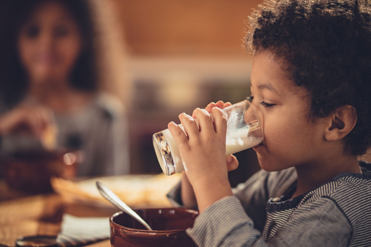 Small black boy drinking fresh milk during breakfast.