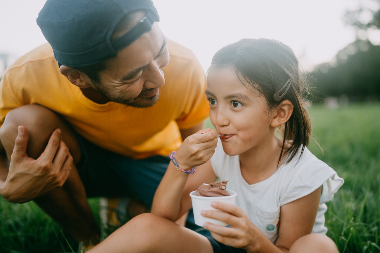 Cheerful young mixed race girl enjoying ice cream with her father in park, Tokyo