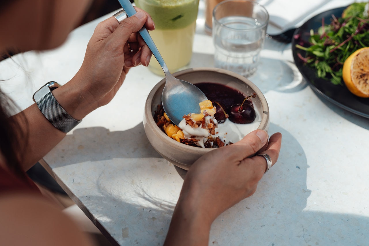 Young woman eating a bowl of fresh yoghurt with cherries and mango for breakfast. Healthy eating and wellbeing concept.
