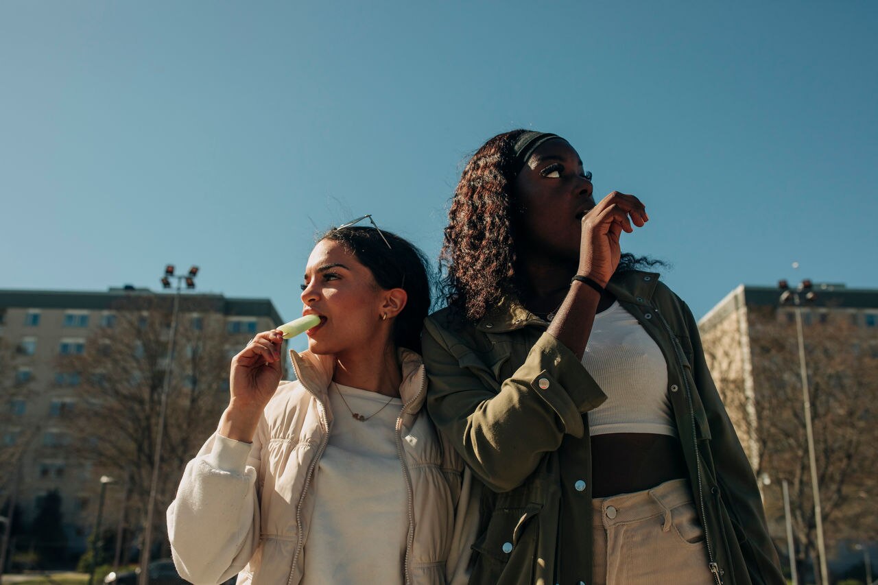 Low angle view of female friends eating ice cream while looking away on sunny day