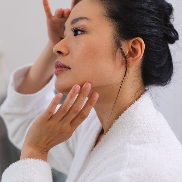 Happy asian woman wearing bathrobe standing in front of mirror applying face cream in bathroom. lifestyle, self care, health and beauty.; Shutterstock ID 2285537035; purchase_order: P&B Loop 1&2(26)-1*.16.01.2024; job: ; client: ; other: 