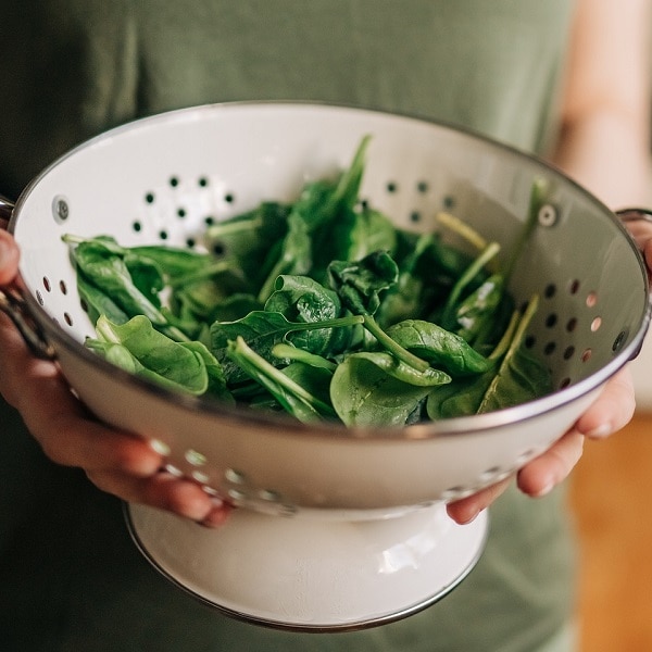 Green vegan breakfast meal in bowl with spinach, arugula, avocado, seeds and sprouts. Girl in leggins holding plate with hands visible, top view. Clean eating, dieting, vegan food concept