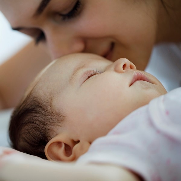 Mother kissing her sleeping newborn baby