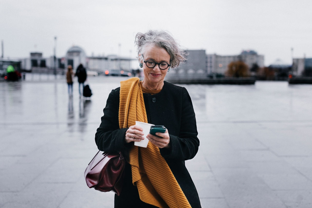 A mature businesswoman siling while texting using her smartphone on her lunchbreak .