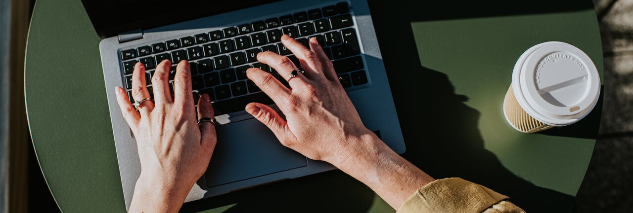Corporate image of hands typing on a laptop keyboard in an outdoor environment, perhaps a balcony, a garden or a rooftop terrace.