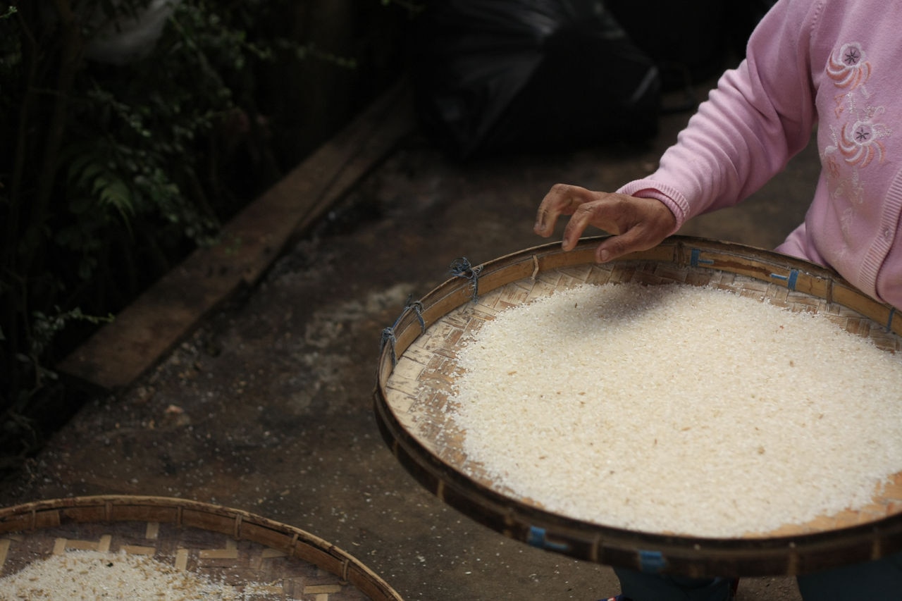 Thai woman sorting and picking out dirt and stones from her rice using a woven bamboo drying rack