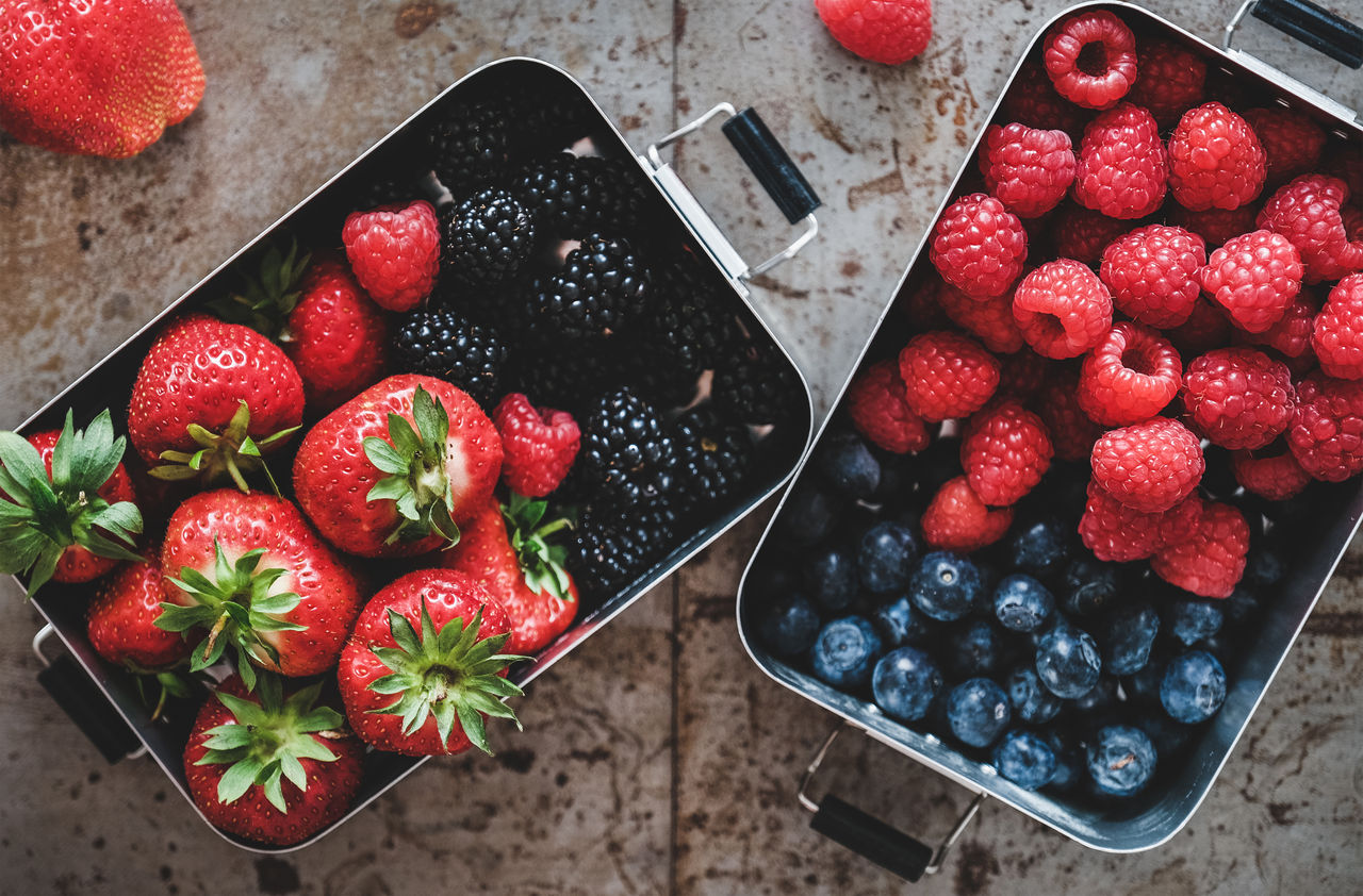 Healthy summer vegan lunch. Flat-lay of fresh seasonal strawberries, raspberries, blueberries and blackberries in lunchboxes over grey background, top view. Vegan, vegetarian, clean eating, detox food